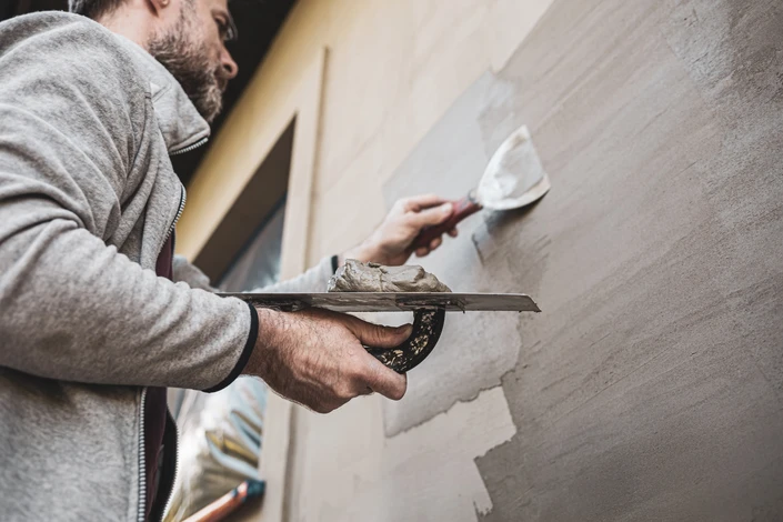Artisan en sweat gris applique de l'enduit ou du mortier sur un mur intérieur avec une taloche métallique