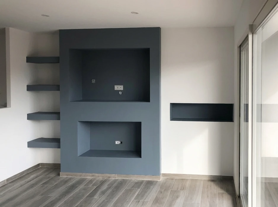 Mur d'accent en plâtre peint gris anthracite mat, avec deux niches rectangulaires encastrées équipées de prises électriques et sortie TV