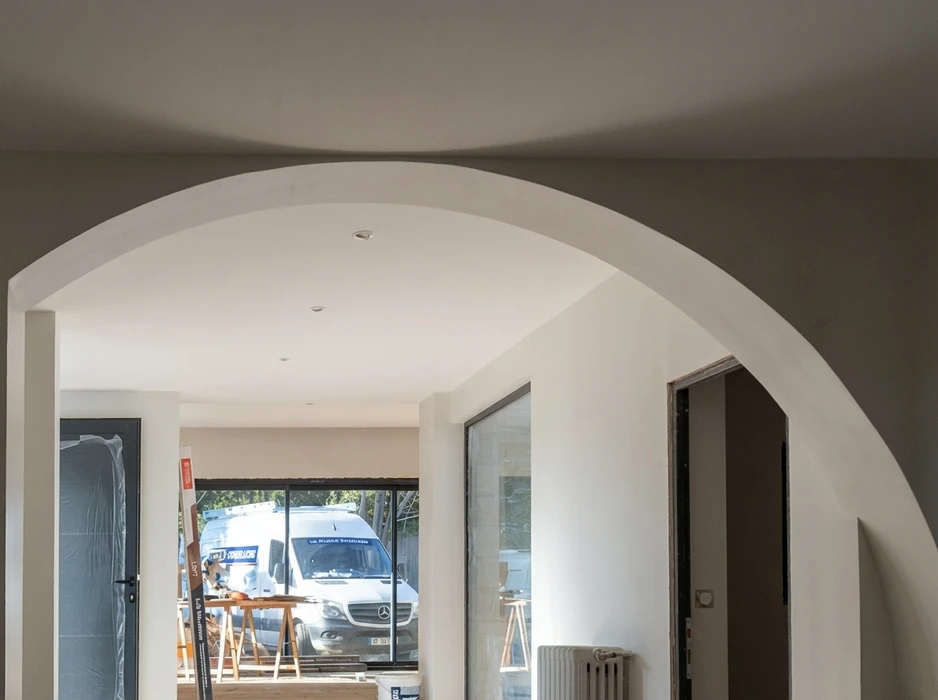 Intérieur en cours de rénovation, vue depuis une pièce vers un couloir lumineux donnant sur l'extérieur
