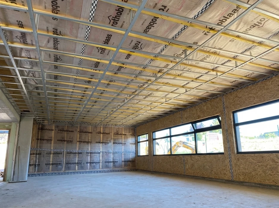 Chantier intérieur d'un bâtiment en ossature bois, murs en panneaux OSB avec pare-vapeur Rothoblaas, faux-plafond métallique en cours de pose sur fourrures