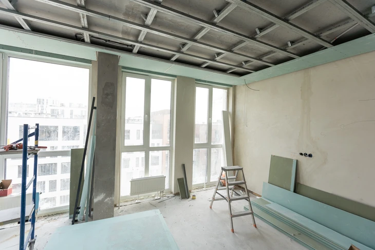 Chantier de rénovation intérieure avec ouvrier en bleu travaillant dans une pièce en cours d'aménagement