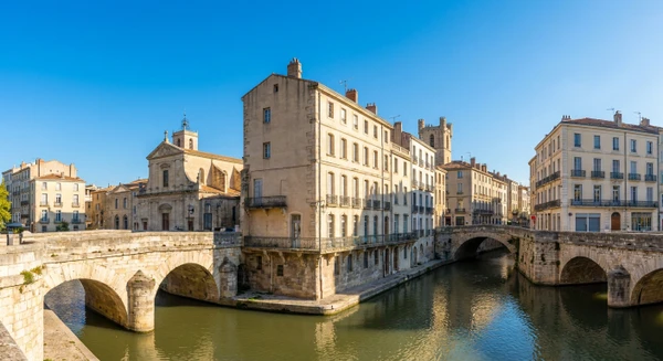 Photographie panoramique ou au niveau du sol de Narbonne, montrant l'architecture urbaine caract&eacute;ristique de la ville avec ses fa&ccedil;ades de b&acirc;timents r&eacute;sidentiels ou commerciaux, repr&eacute;sentatifs du tissu urbain o&ugrave; intervient l'entreprise de pl&acirc;trerie et r&eacute;novation int&eacute;rieure. La perspective doit clairement montrer le type de constructions (immeubles anciens ou modernes) accessibles aux services de pl&acirc;trerie, isolation et am&eacute;nagement int&eacute;rieur. Image sans texte, logo ou filigrane visible.