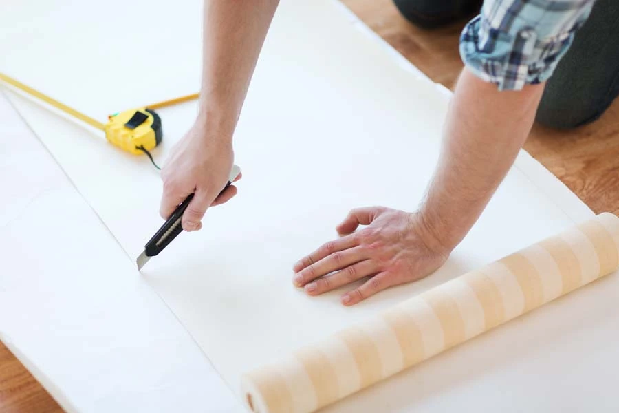 Homme travaillant à genoux sur plancher intérieur, découpant matériau isolant blanc avec cutter