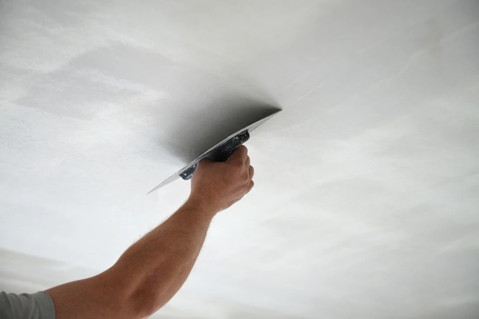 Ouvrier en bâtiment appliquant de l'enduit sur un mur intérieur avec une taloche